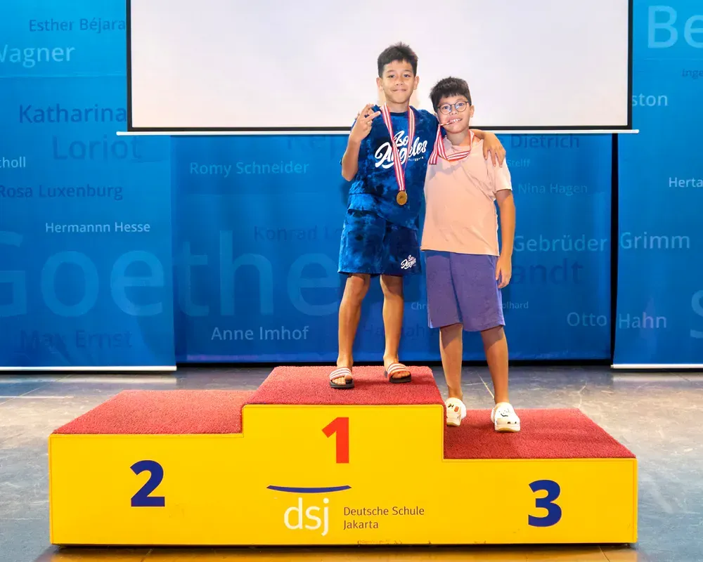 Two young boys are standing on a podium holding medals.