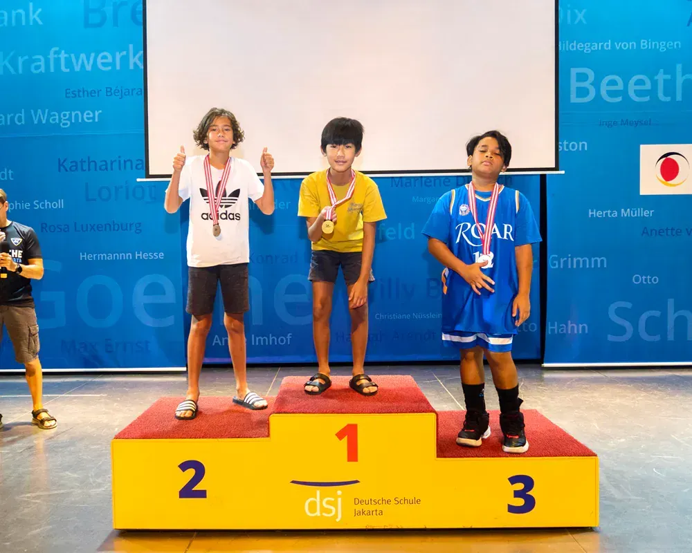 Three young boys are standing on a podium with the number 1 on it