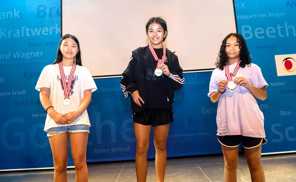 Three girls are standing next to each other with medals around their necks.