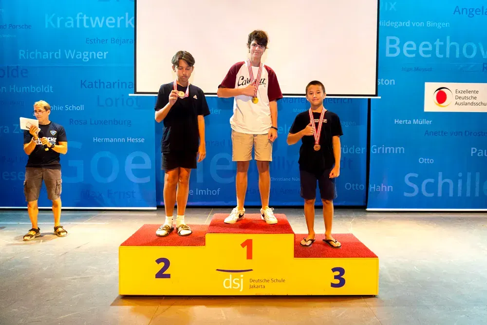 Three boys are standing on a yellow podium with the number 1 on it