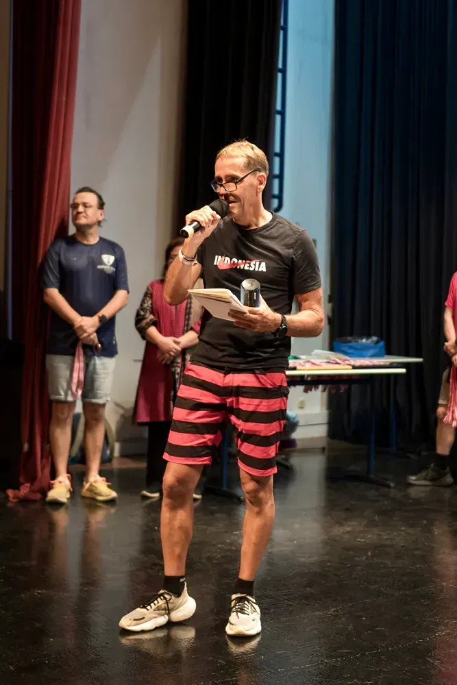 A man in striped shorts is standing on a stage holding a microphone.