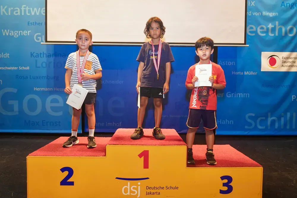 Three children are standing on a podium with the number 1 on it