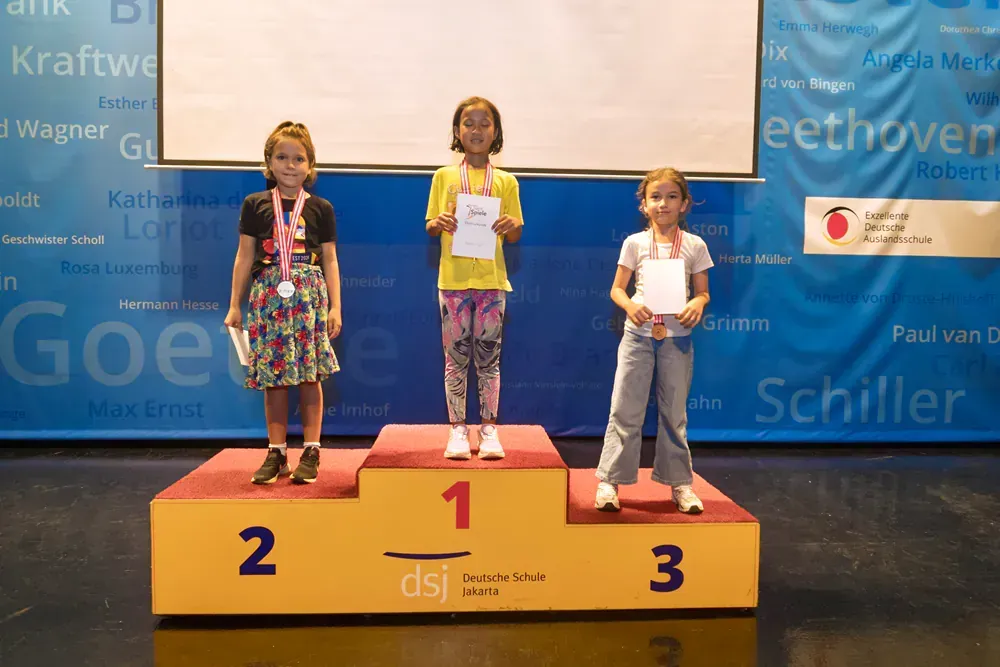 Three young girls are standing on a podium holding awards.