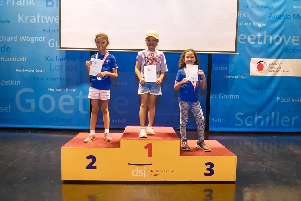 Three young girls are standing on a podium holding certificates.