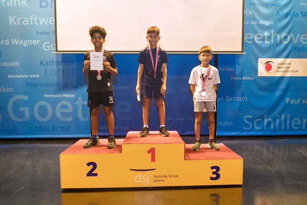Three young boys are standing on a podium holding medals.