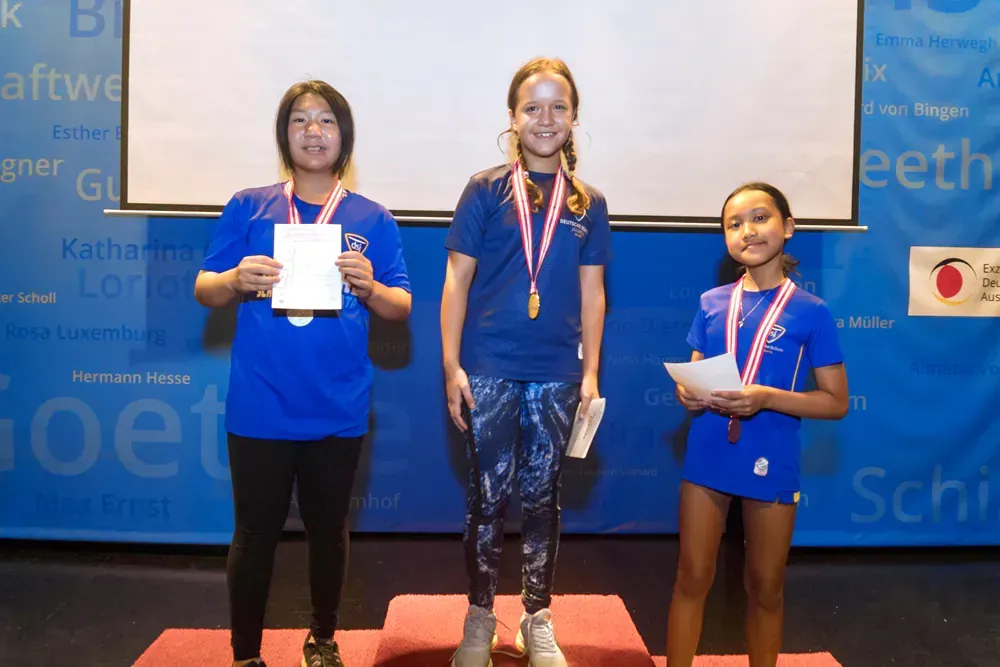 Three young girls are standing on a podium with medals around their necks.