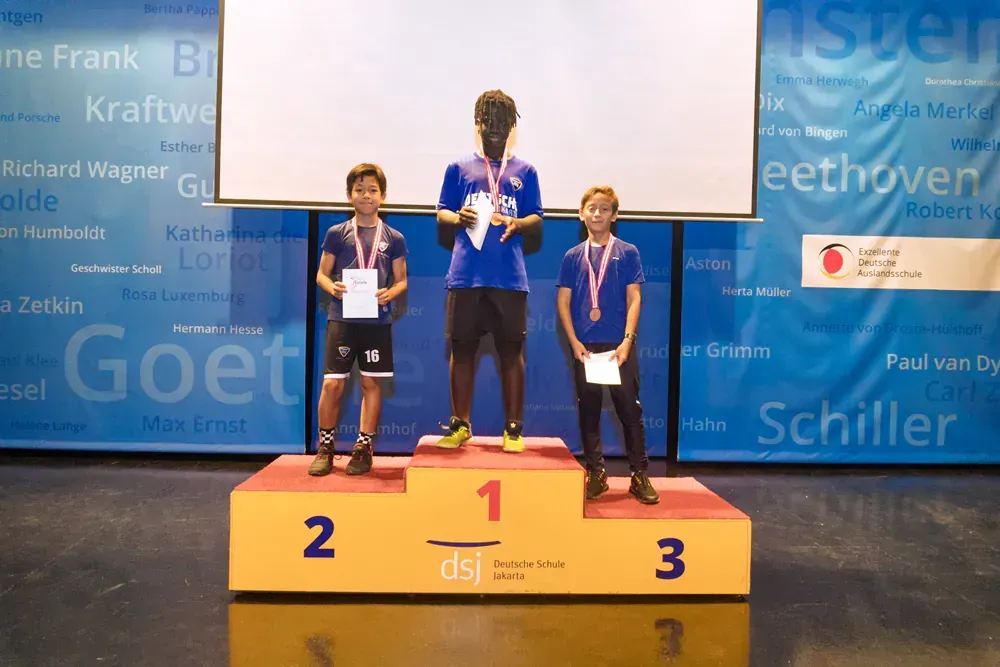 Three boys are standing on a podium with the number 1 on it