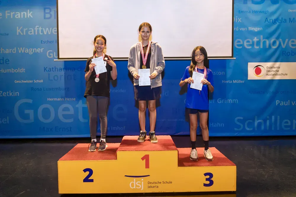 Three girls are standing on a podium with the number 1 on it
