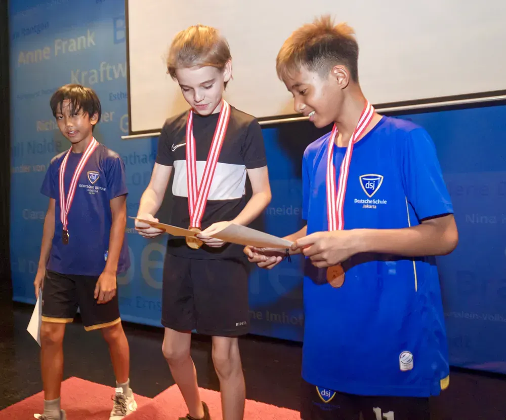Three young boys wearing medals are standing on a stage