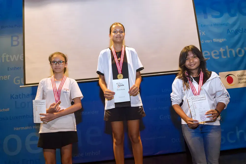 Three girls are standing on a stage holding medals and certificates.