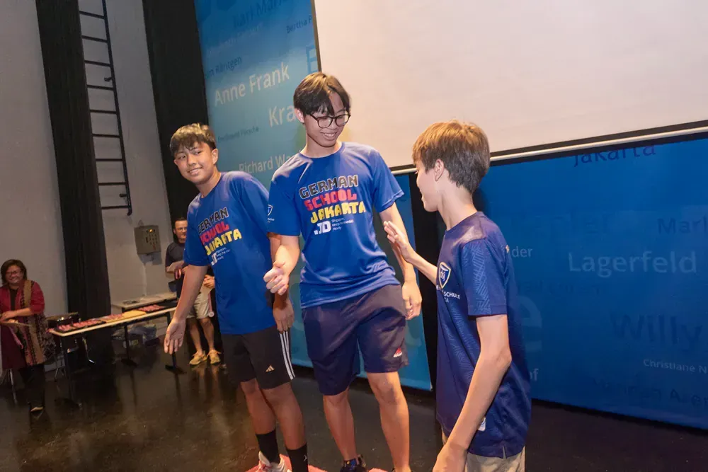 A group of young men are standing on a stage in front of a large screen.