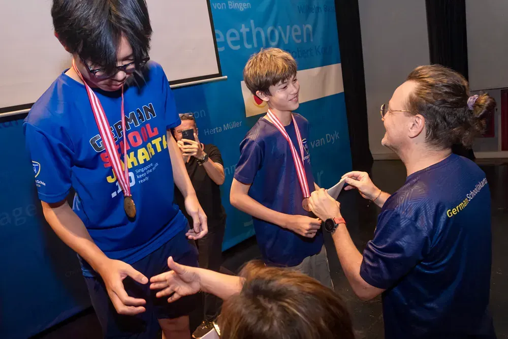 A man is giving a medal to a boy in a blue shirt.