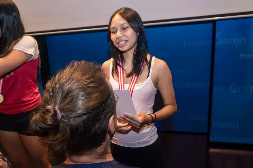 A woman wearing a medal is standing in front of a blue wall.