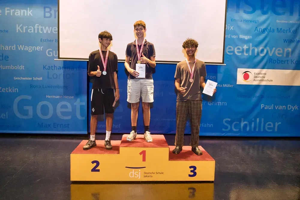 Three young men are standing on a podium holding medals.