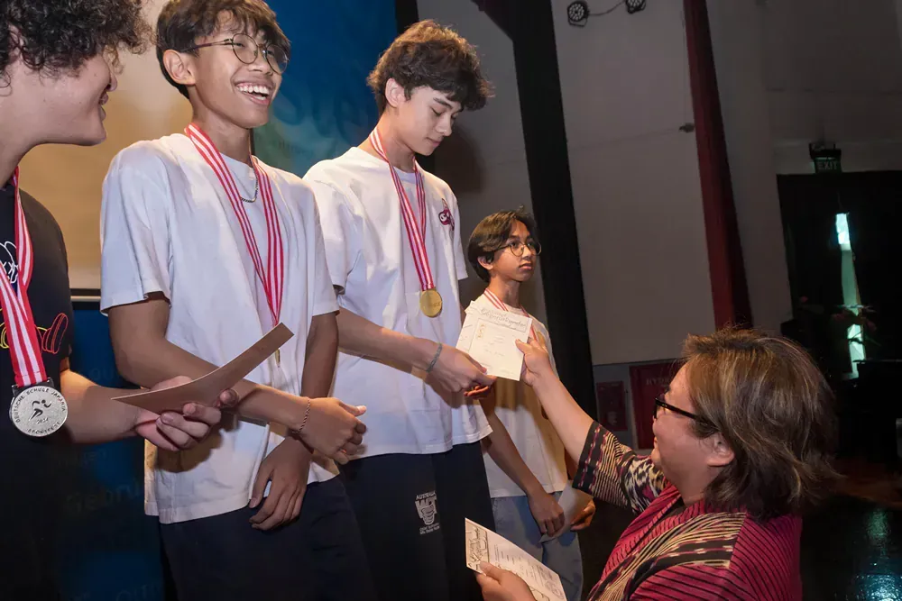 A woman is giving a certificate to two boys who are wearing medals.