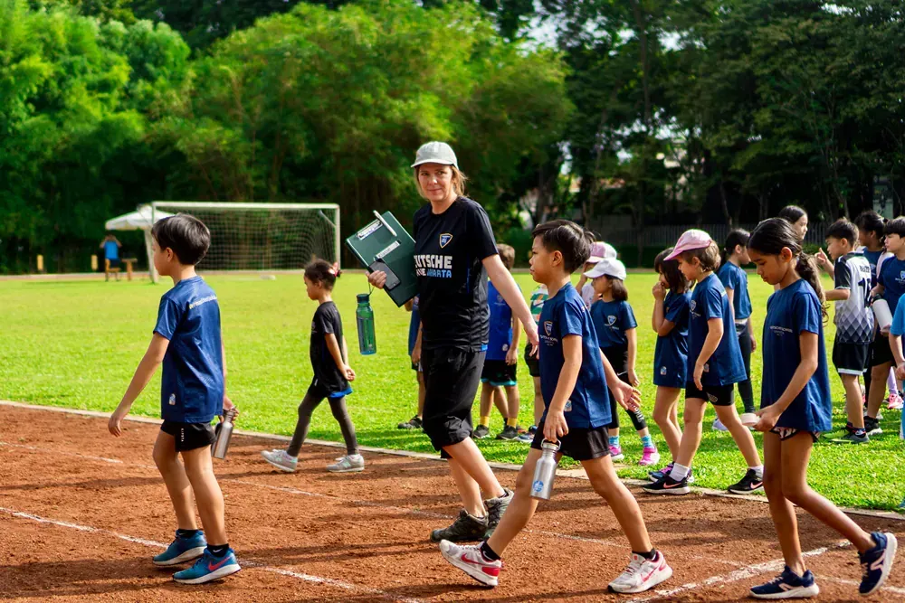 A group of children are walking on a track with a coach.