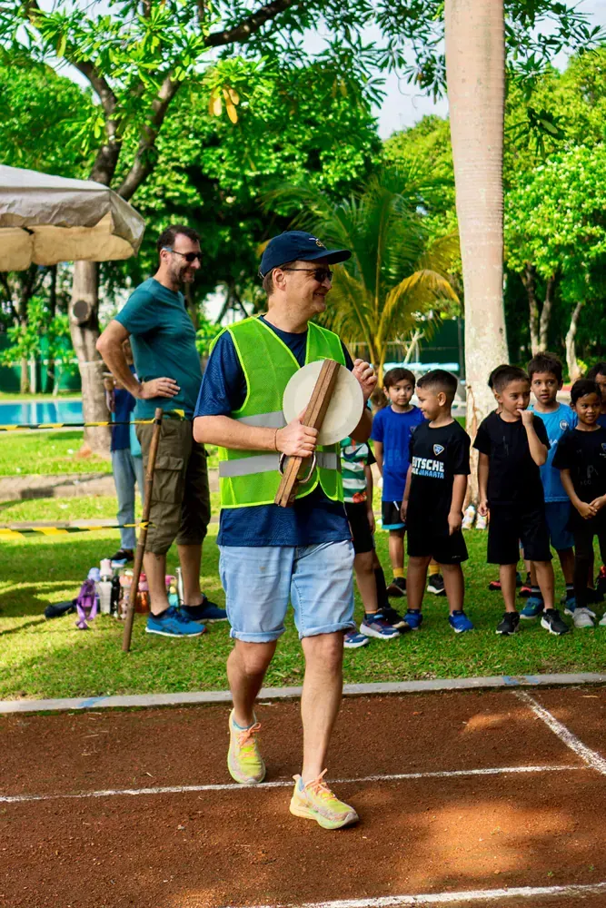 A man in a yellow vest is walking on a track holding a drum.