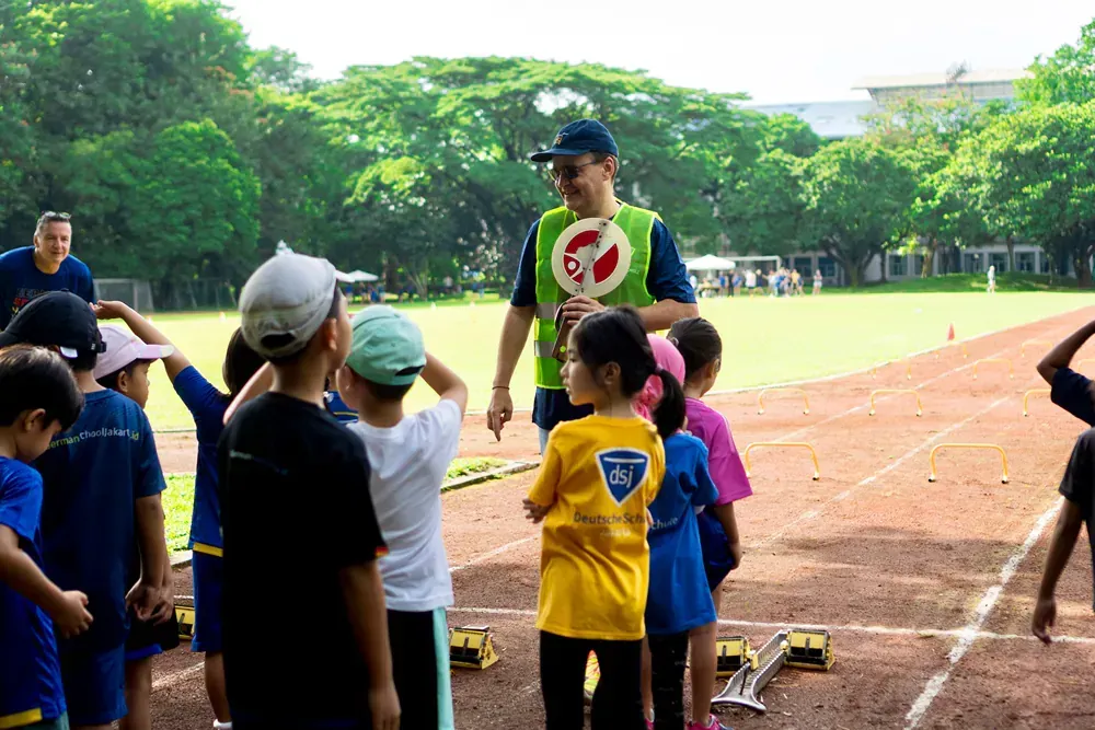 A group of children are standing on a track with a man holding a sign that says no.