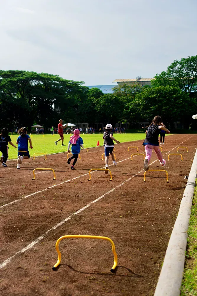 A group of children are running on a track with hurdles.