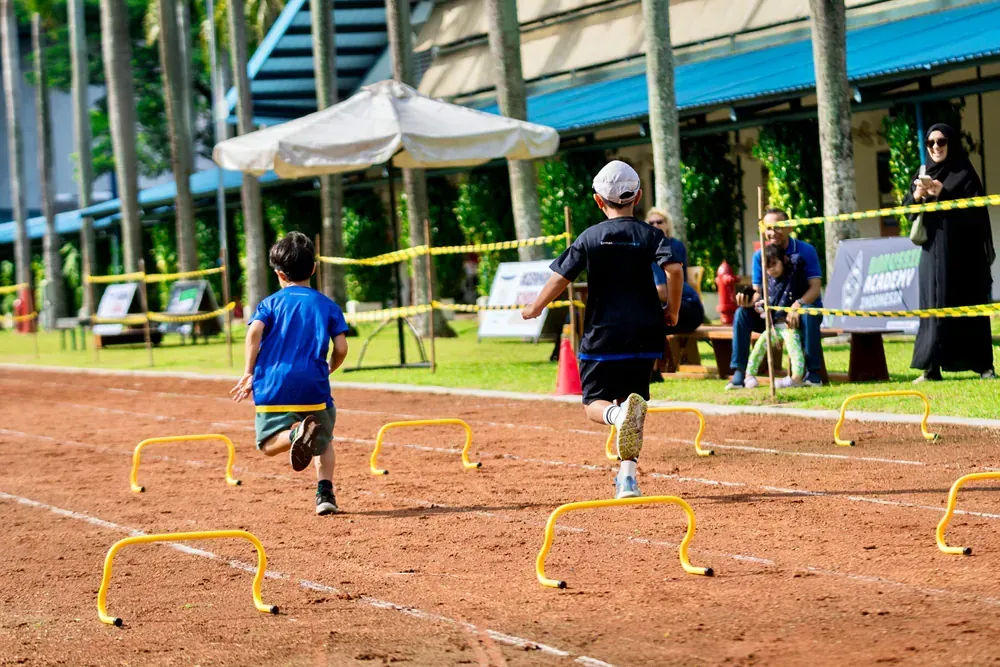 A group of children are running over hurdles on a dirt track.