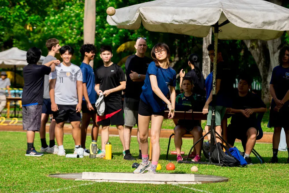 A group of people are watching a woman throw a ball on a field.