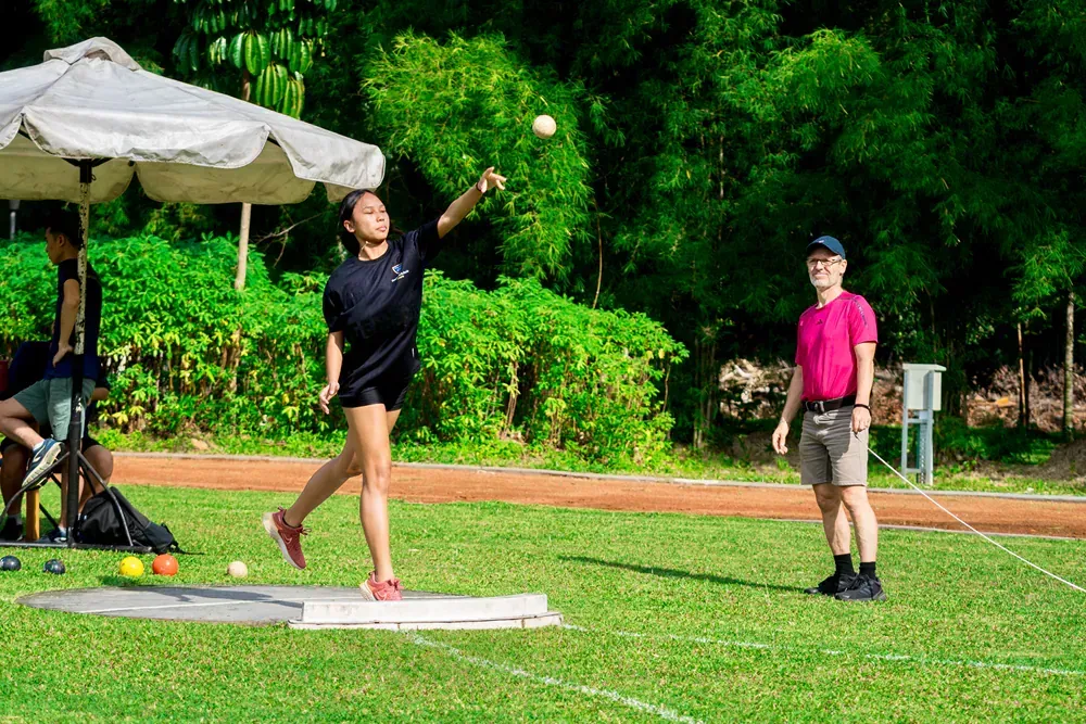 A woman is throwing a ball on a field while a man watches.
