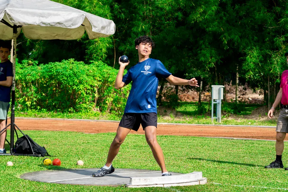 A young boy is throwing a shot put ball on a field.