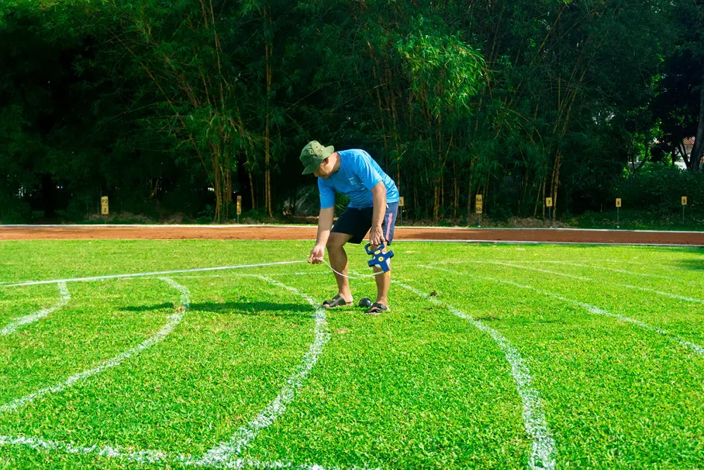 A man is kneeling on a lush green field with white lines drawn on it.