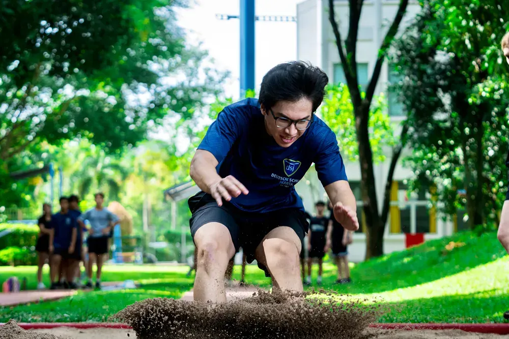 A man is jumping in the dirt in a park.