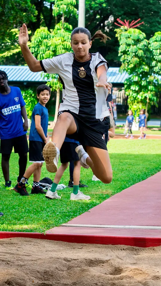 A young girl is jumping in the air while competing in a long jump competition.