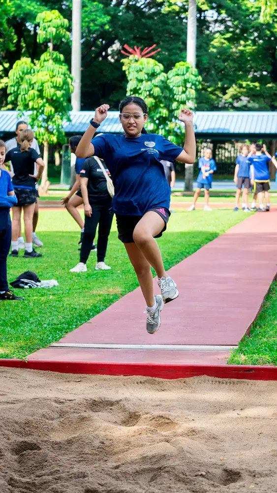 A young girl is jumping in the air while competing in a long jump competition.