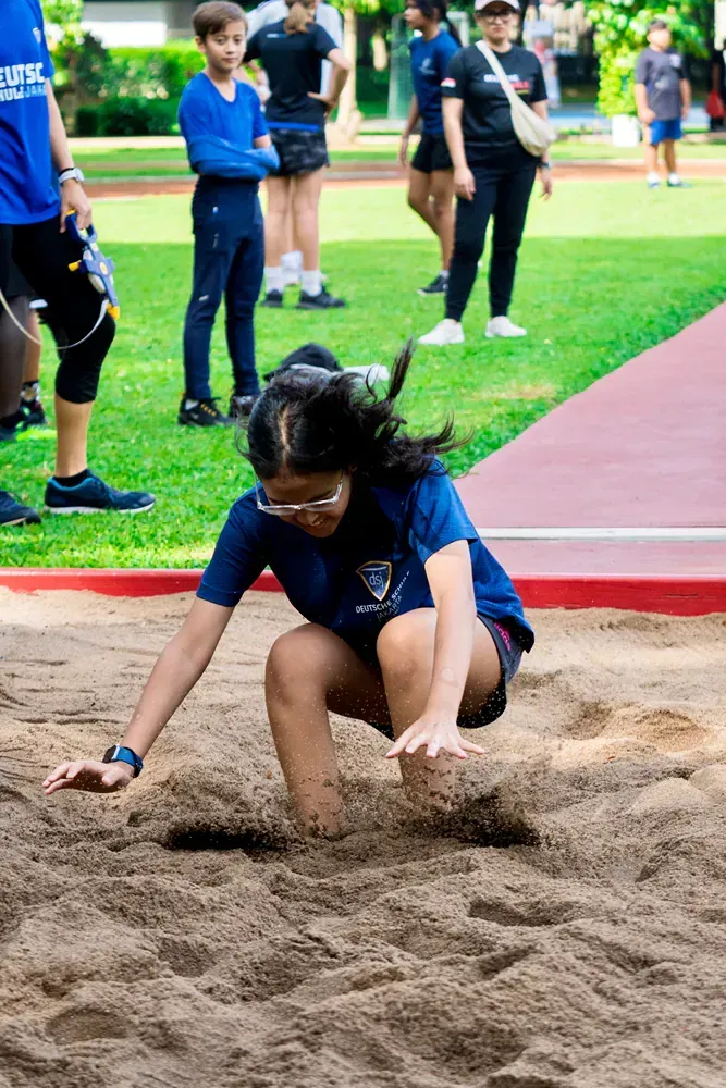 A young girl is kneeling in the sand on a track.