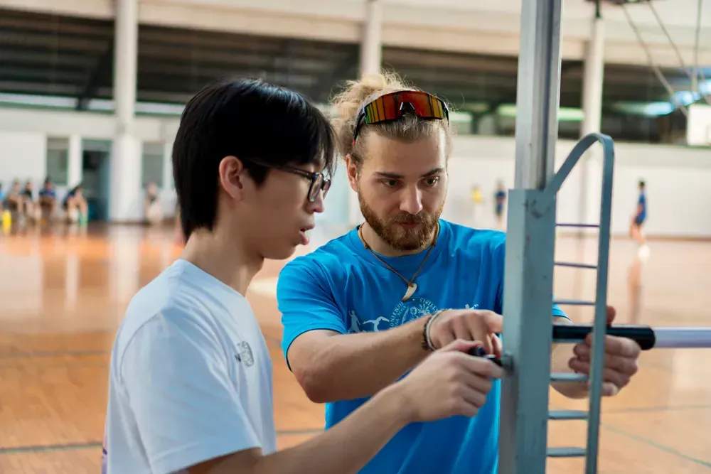 A man in a blue shirt is teaching a young man how to use a machine.
