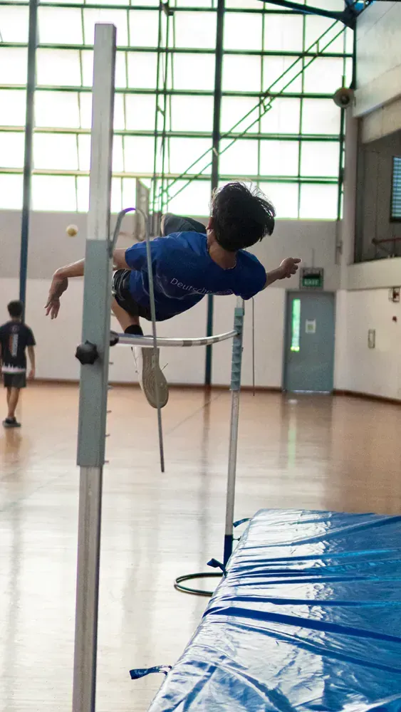 A young boy is jumping over a bar in a gym.
