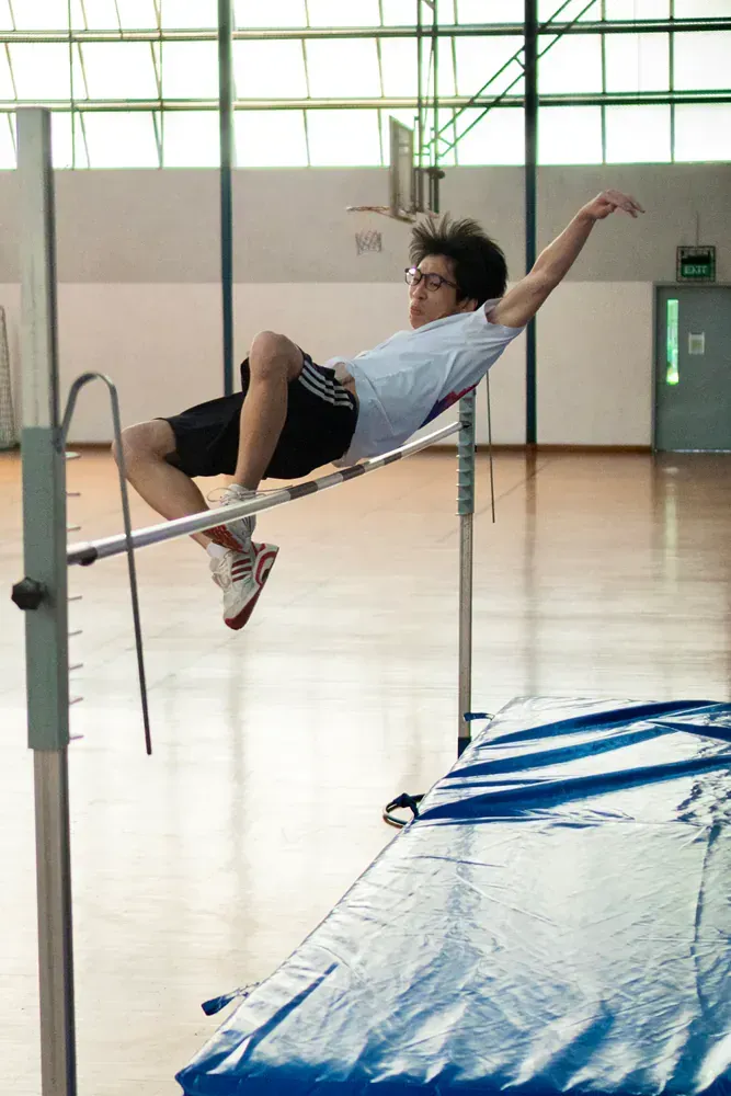 A young man is jumping over a bar in a gym.