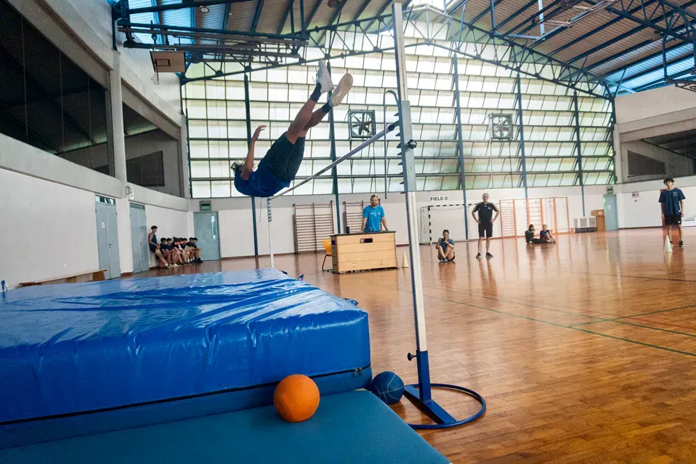 A person is jumping over a bar in a gym.