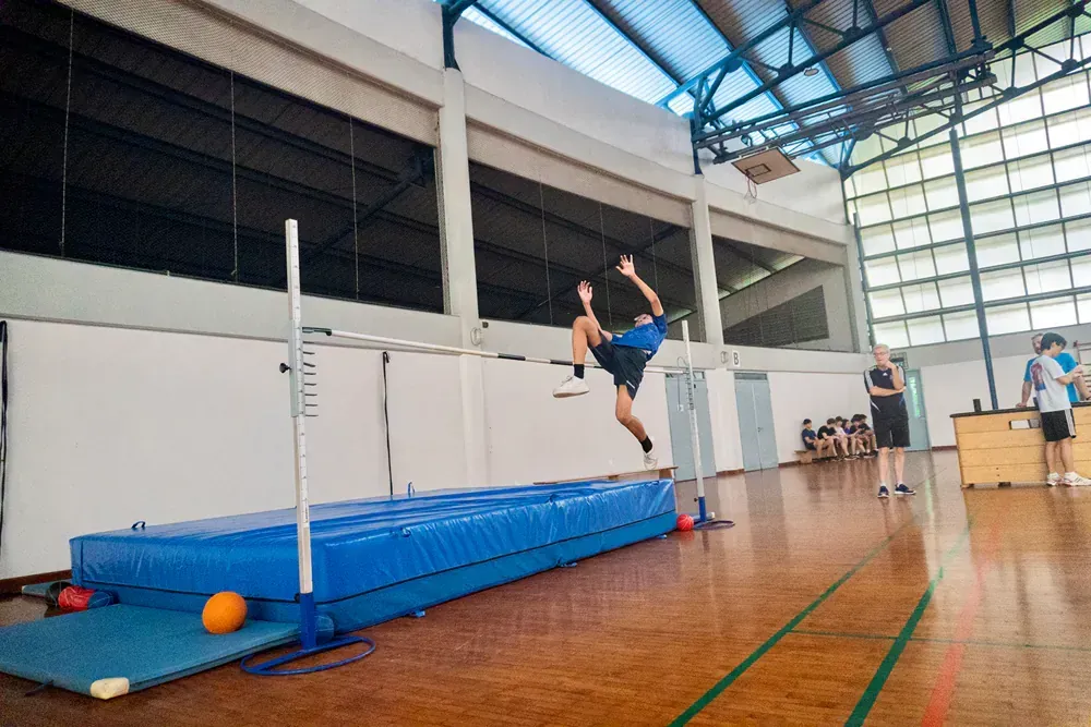 A person is jumping over a bar in a gym.