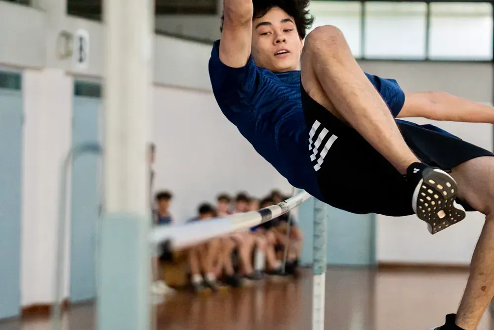 A young man is jumping over a pole in a gym.