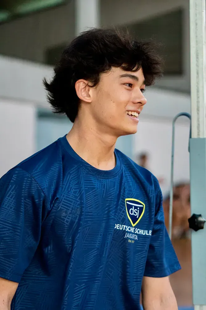 A young man is wearing a blue t-shirt and smiling.