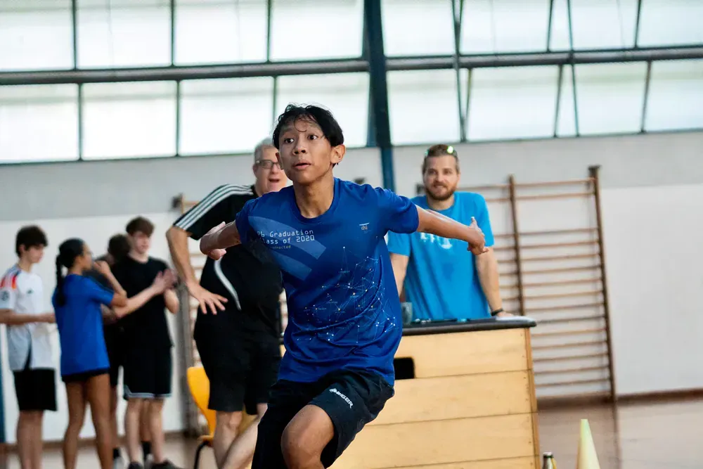 A young boy is jumping over a wooden box in a gym.