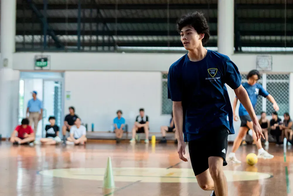 A young man is running with a soccer ball in a gym.
