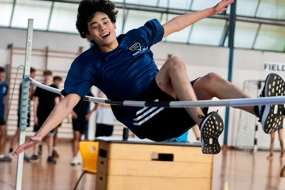 A young man is jumping over a bar in a gym.