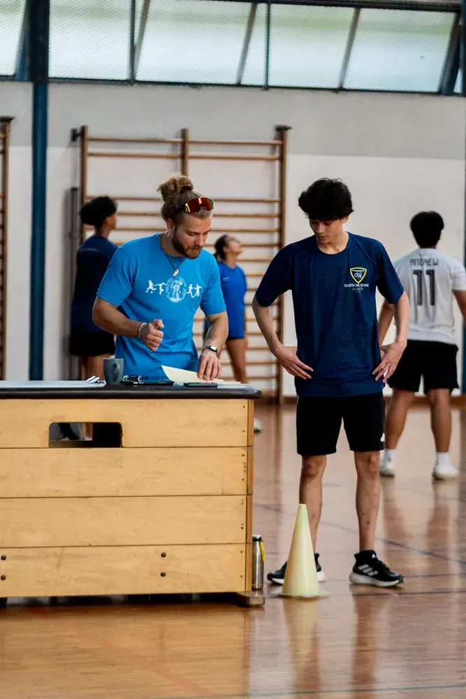 A man in a blue shirt is writing on a piece of paper in a gym.