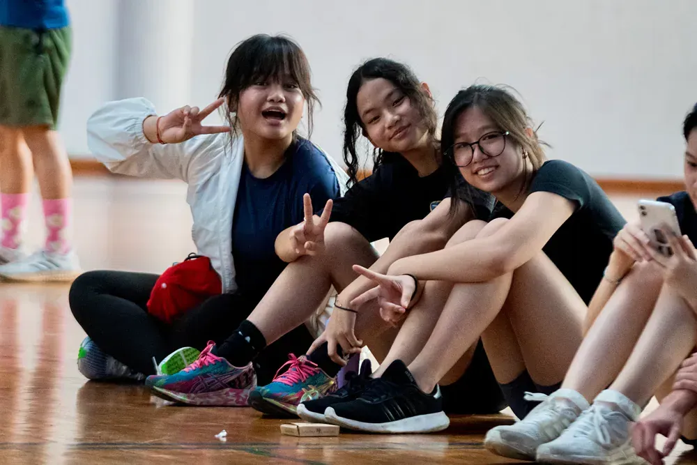A group of young girls are sitting on the floor making peace signs.