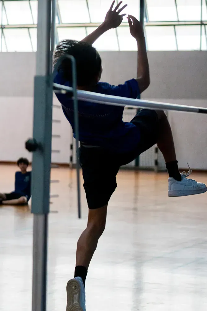 A boy in a blue shirt is jumping over a bar