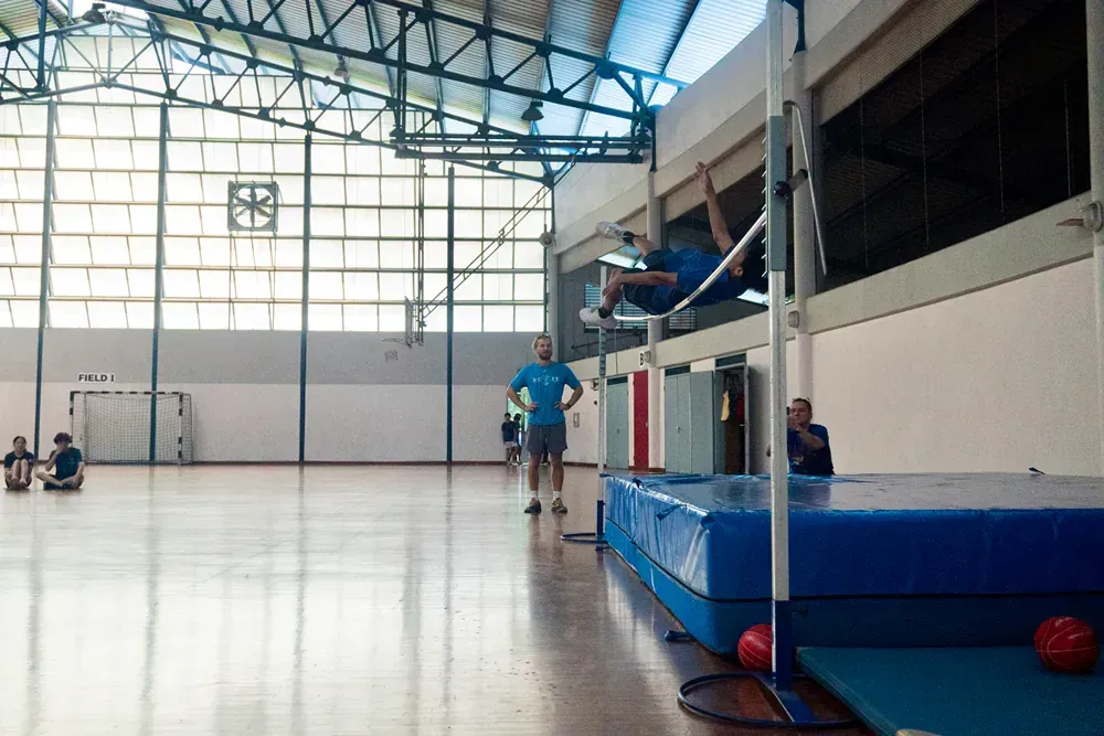 A man is jumping over a bar in a gym.
