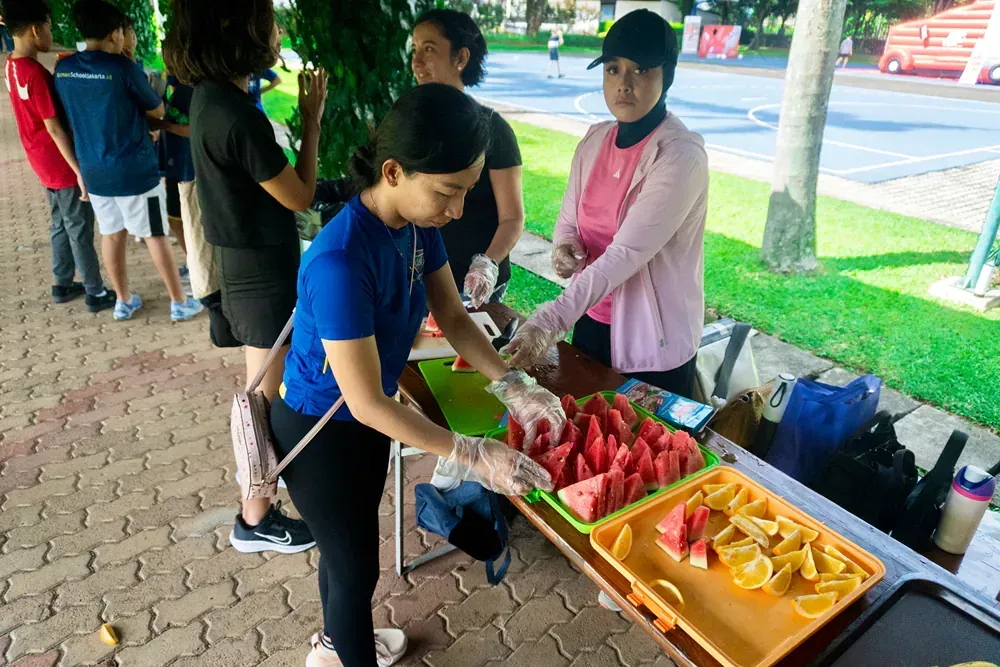 A woman is cutting watermelon at a table with other people.