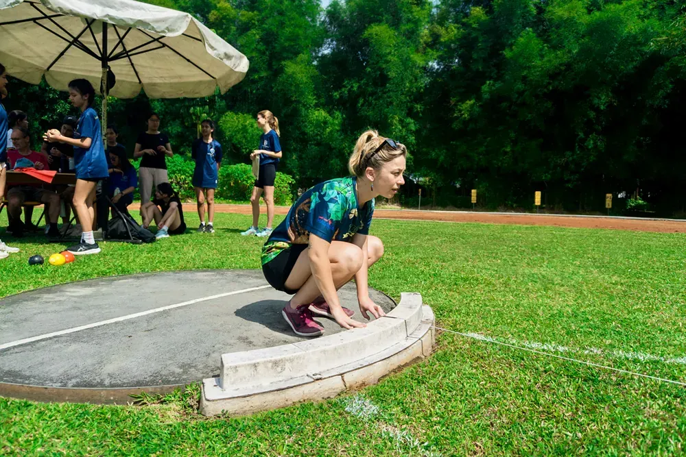 A young girl is squatting down on a track to throw a discus.