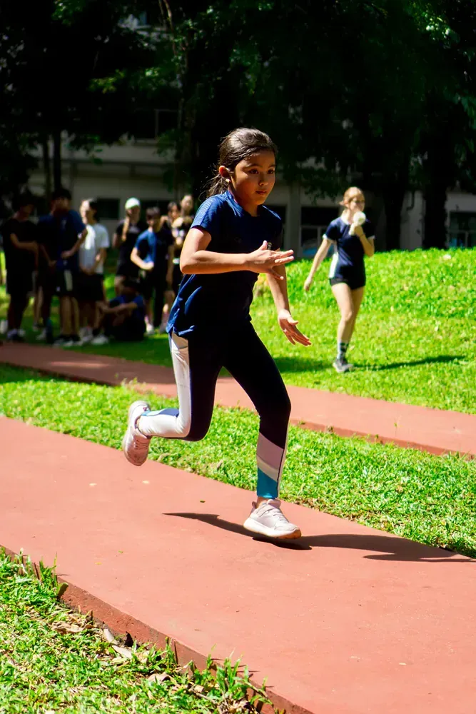 A young girl is running on a track in a park.