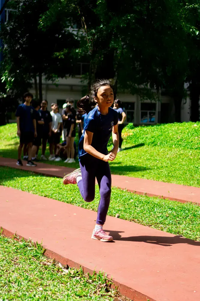 A young girl is running on a track in a park.